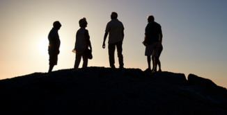 Silhouette of four people atop a hill.